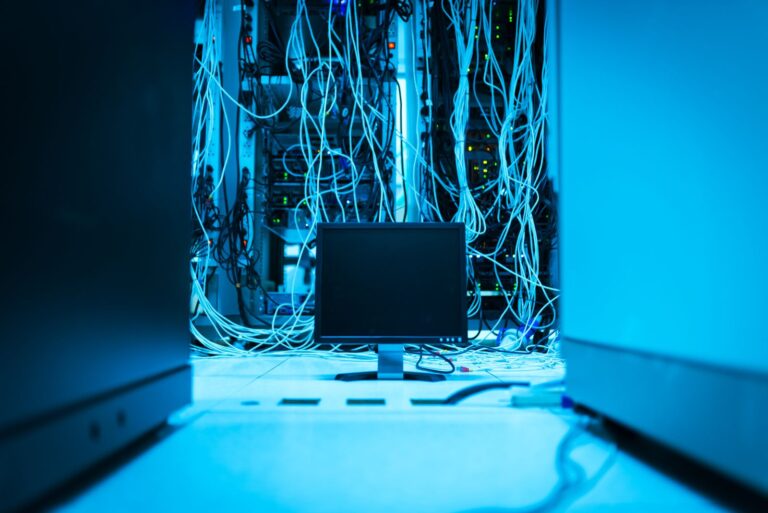 Serverschränke mit dichter Netzwerkverkabelung und einem Monitor in blauem Licht